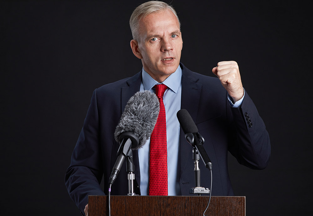 passionate-mature-man-giving-speech-at-podium-M3KL8V7